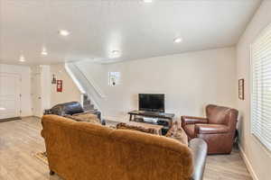 Living room with a textured ceiling, light wood-type flooring, baseboards, recessed lighting, and stairway
