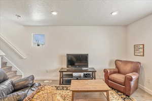 Living room with stairway, baseboards, light wood-style floors, and a textured ceiling