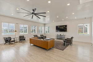 Living room featuring baseboards, a ceiling fan, light wood finished floors, and recessed lighting