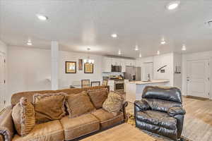 Living area with recessed lighting, light wood-style floors, baseboards, a textured ceiling, and a notable chandelier