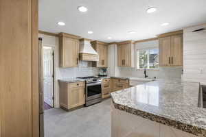 Kitchen with light stone counters, a sink, decorative backsplash, stainless steel electric range, and custom range hood
