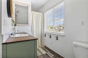 Bathroom featuring wood finished floors, vanity, baseboards, toilet, and visible vents
