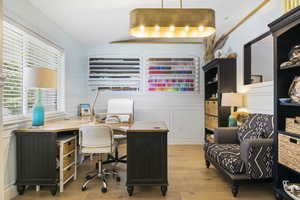 Office area with light wood-type flooring, a wainscoted wall, and vaulted ceiling