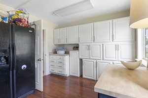 Kitchen with butcher block counters, dark wood-style flooring, white cabinetry, and black fridge