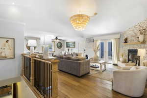 Living room with a fireplace, ceiling fan with notable chandelier, and light wood-type flooring