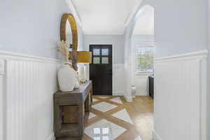 Entrance foyer featuring wainscoting, light wood-style flooring, and arched walkways