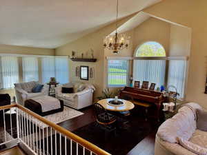 Living room with vaulted ceiling, wood finished floors, and an inviting chandelier