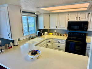 Kitchen with black appliances, a sink, white cabinets, and light countertops