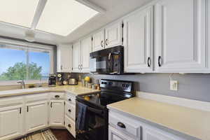 Kitchen with a textured ceiling, a sink, light countertops, black appliances, and white cabinetry