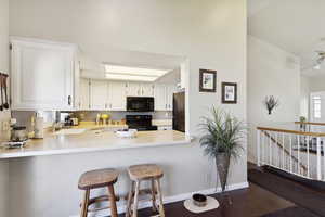 Kitchen with a sink, light countertops, white cabinets, black appliances, and dark wood-type flooring