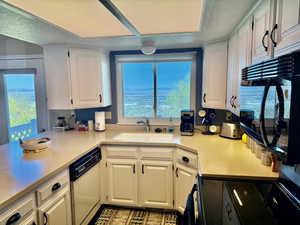 Kitchen with a wealth of natural light, a sink, white cabinetry, white dishwasher, and light countertops with gorgeous view