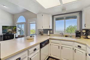 Kitchen with dishwasher, a sink, light countertops, a peninsula, and white cabinetry