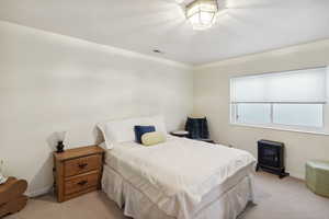 Bedroom with light colored carpet, a wood stove, baseboards, and visible vents
