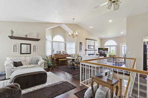 Living area with lofted ceiling, dark wood-style floors, recessed lighting, a tiled fireplace, and ceiling fan with notable chandelier