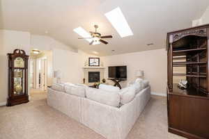 Living area featuring lofted ceiling with skylight, a fireplace, and ceiling fan