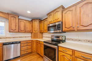 Kitchen with decorative backsplash, brown cabinets, light wood-style flooring, stainless steel appliances, and light countertops
