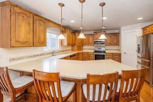 Kitchen with stainless steel appliances, a kitchen breakfast bar, backsplash, and brown cabinetry