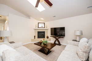 Carpeted living area with a tiled fireplace,  lofted ceiling with skylight, and ceiling fan