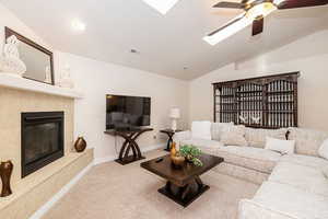 Living room featuring a high end fireplace, vaulted ceiling with skylight, carpet flooring, and a ceiling fan