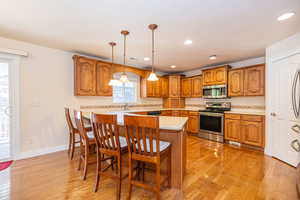 Kitchen featuring brown cabinets, stainless steel appliances, light countertops, a kitchen bar, and decorative light fixtures
