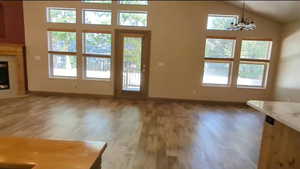 Unfurnished living room featuring light wood-type flooring, healthy amount of natural light, baseboards, and lofted ceiling