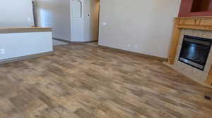 Unfurnished living room featuring wood finished floors, a tiled fireplace, and baseboards