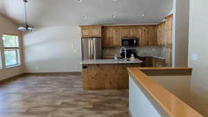 Kitchen featuring appliances with stainless steel finishes, a sink, light wood-style flooring, an island with sink, and a chandelier