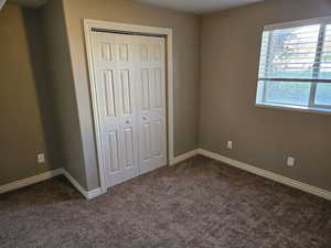 Unfurnished bedroom with dark colored carpet, baseboards, and a closet
