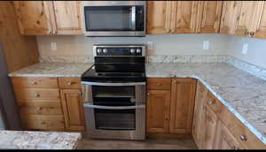 Kitchen featuring stainless steel appliances, light stone countertops, wood finished floors, and brown cabinetry