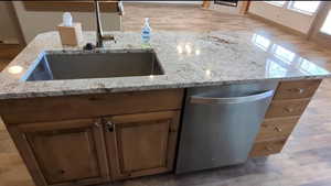 Kitchen view of a sink, dishwasher, light stone counters, and wood finished floors