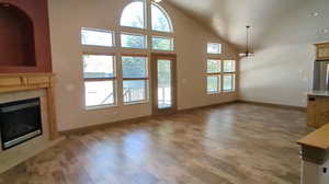 Unfurnished living room featuring healthy amount of natural light, light wood-type flooring, baseboards, and high vaulted ceiling