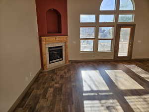 Unfurnished living room featuring baseboards, a tile fireplace, a healthy amount of sunlight, and dark wood-style floors