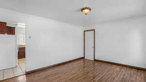 Empty room with baseboards, crown molding, and light wood-style floors