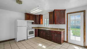 Kitchen with baseboards, under cabinet range hood, a sink, and white appliances