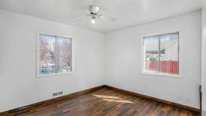 Empty room with dark wood finished floors, visible vents, baseboards, and a healthy amount of sunlight