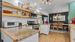 Kitchen with a peninsula, light wood-style floors, a chandelier, open shelves, and appliances with stainless steel finishes