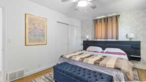 Bedroom with wood finished floors, wallpapered walls, a closet, baseboards, and visible vents