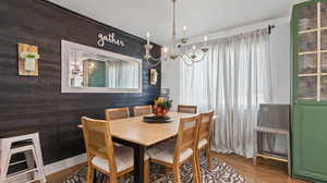 Dining room with wood finished floors, wood walls, and a notable chandelier