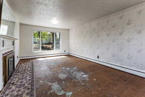 Unfurnished living room featuring a glass covered fireplace, baseboard heating, baseboards, and a textured ceiling