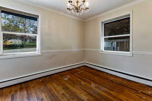 Main floor bedroom featuring a baseboard heating unit, an inviting chandelier, ornamental molding, and original wood flooring.