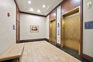 Hallway featuring tile patterned flooring, elevator, a tray ceiling, and recessed lighting