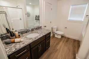 Full bathroom with toilet, baseboards, wood finished floors, a shower with shower curtain, and vanity