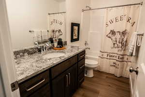 Bathroom with wood finished floors, toilet, vanity, and shower / bath combination with curtain