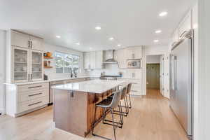 Kitchen with a breakfast bar, light wood-type flooring, wall chimney range hood, and built in appliances