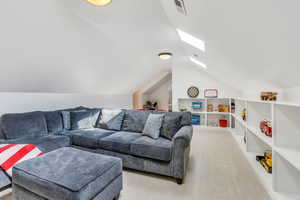 Carpeted living room with vaulted ceiling with skylight and visible vents