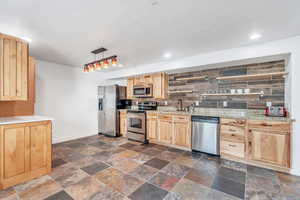 Kitchen featuring stone tile floors, stainless steel appliances, and light brown cabinetry