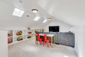 Playroom with visible vents, built in shelves, carpet flooring, and vaulted ceiling with skylight