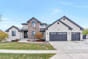 View of front facade featuring stucco siding, concrete driveway, stone siding, a front yard, and a garage