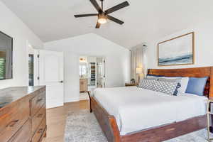 Bedroom featuring connected bathroom, vaulted ceiling, a ceiling fan, and light wood-type flooring