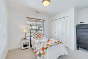 Bedroom with light colored carpet, baseboards, visible vents, and a closet